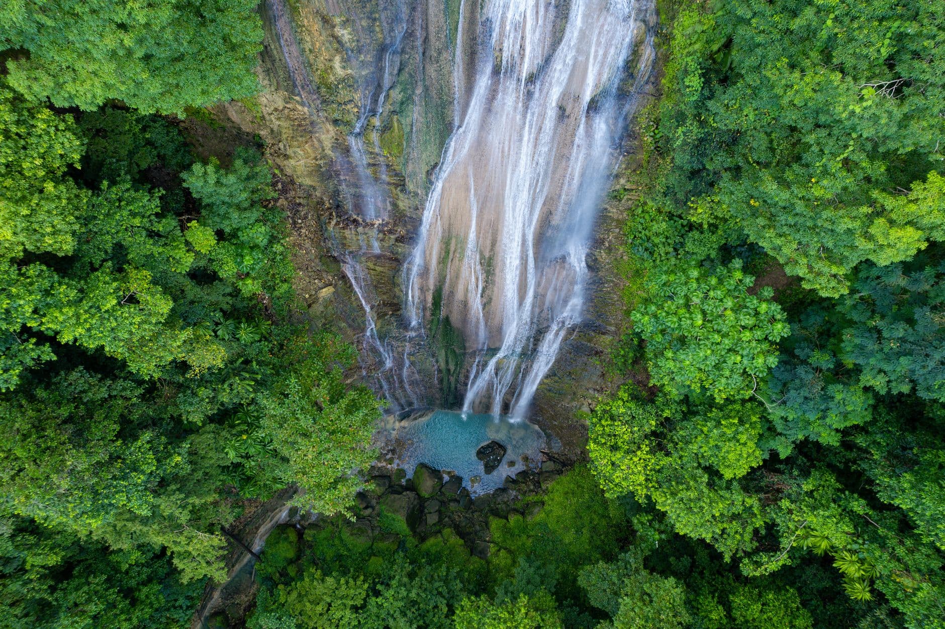 Stunning aerial view of a lush Jamaican waterfall surrounded by verdant jungle foliage.